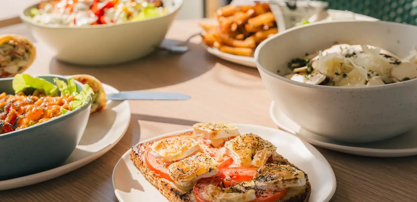Des bowls garnis, des wraps et une assiette de frites partagés sur une table en bois